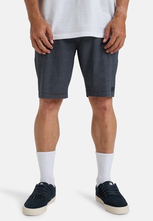 Pantalones cortos deportivos grises con una textura sutil, presentando un parche con el logo negro. Combinados con calcetines blancos y zapatillas de deporte azul marino.