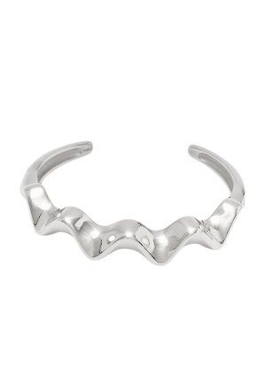 Bracciale in argento con un design scultoreo ondulato e estremità aperte, che riflette la luce su uno sfondo bianco.