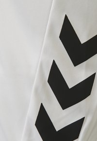 Vit tyg med ett framträdande svart zigzag-mönster. Texturen verkar slät med en lätt glans, vilket skapar en modern designelement.