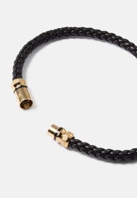 Bracelet en cuir tressé noir avec des fermoirs magnétiques en tonalité dorée sur un fond blanc uni.