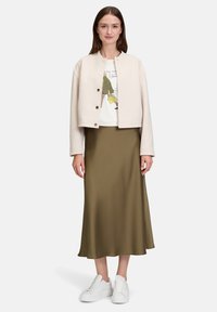 Damski strój z kremową kurtką bomberką, białym t-shirtem z grafiką, oliwkową satynową spódnicą i białymi trampkami.