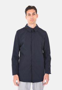 Cappotto impermeabile navy con chiusura a bottoni, colletto alto e due tasche laterali. Realizzato in tessuto liscio, presenta un design minimale.