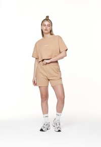 Beige kortærmet t-shirt og matchende shorts lavet af blød bomuld. Toppen har et trykt logo, har en afslappet pasform og elastisk talje.