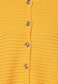 Gelber gerippter Cardigan mit silbernen Knöpfen vorne. Die Textur sieht weich aus und hat ein Strickmuster.