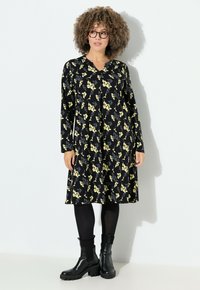 Musta mekko, jossa on keltainen kukkakuosi, pitkät hihat, nappikiinnitys ja rento malli. Yhdistetty mustiin nilkkureihin ja legginsseihin.
