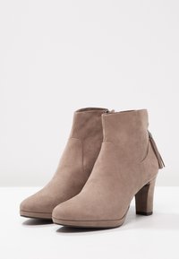 Taupe Wildlederstiefeletten mit dicker Sohle, seitlichem Reißverschluss und dekorativem Quast am Absatz, glatte Textur, abgerundete Zehen.
