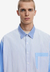 Gestreifte Hemd mit Knopfleiste, das hellblaue und weiße vertikale Streifen, einen hellblauen Kragen und eine kontrastierende Tasche aufweist. Glattes Baumwollgewebe.