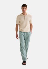 Polo à manches courtes de couleur crème avec une finition texturée, associé à un pantalon ample vert menthe et des sandales noires.