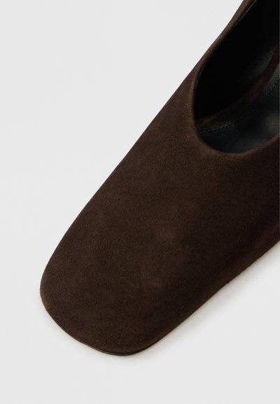 Brūni zamšādas apavi ar kvadrātveida purngalu un noapaļotu griezumu. Gluda tekstūra, minimālistisks stils un bez redzamām detaļām vai akcentiem.