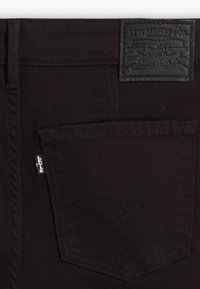 Zwarte denim jeans met een gestructureerd leren label op de tailleband, een opvallend ontwerp voor de achterzak en kenmerkende stiksels.
