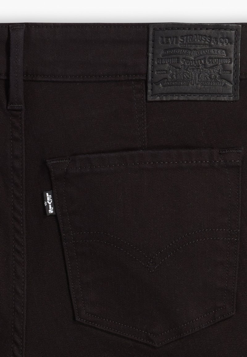 Jean en denim noir avec une étiquette en cuir texturée à la taille, un design distinct des poches arrière et un détail de couture signature.