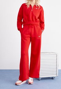 Röd zip-tröja och matchande joggers i mjukt material, med Nike-logotyp. Löst sittande med fickor och dragsko i midjan.