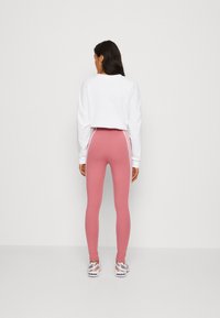 Sweatshirt branco cropped sobre leggings rosas com riscas laterais brancas, apresentando um design ajustado e uma textura de tecido suave, combinado com sapatos desportivos.