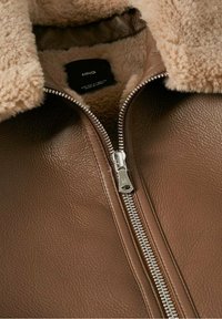 Giubbotto in pelle marrone con finitura testurizzata, dotato di un morbido colletto in shearling beige e una zip argentata lungo la parte anteriore.