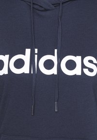 Mörkblå hoodie tillverkad av en bomullsblandning, med en stor vit "adidas"-logotyp på framsidan, med dragsnören och metalltips.