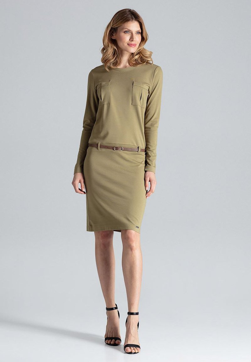 Oliwkowa sukienka z długim rękawem, z dwiema kieszeniami na piersi, dopasowany krój, podkreślona brązowym pasem, noszona z czarnymi sandałkami na obcasie.