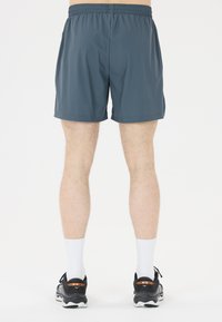 Herrarnas träningsshorts i mörkgrått, i polyester, med elastisk midja, knälängd, tillsammans med svarta löparskor och vita strumpor.