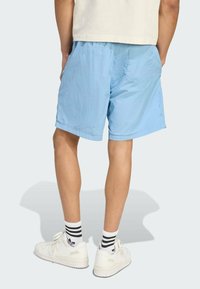 Light blue shorts made of lightweight fabric, featuring an elastic waistband and a back pocket. Worn with white sneakers and striped socks.