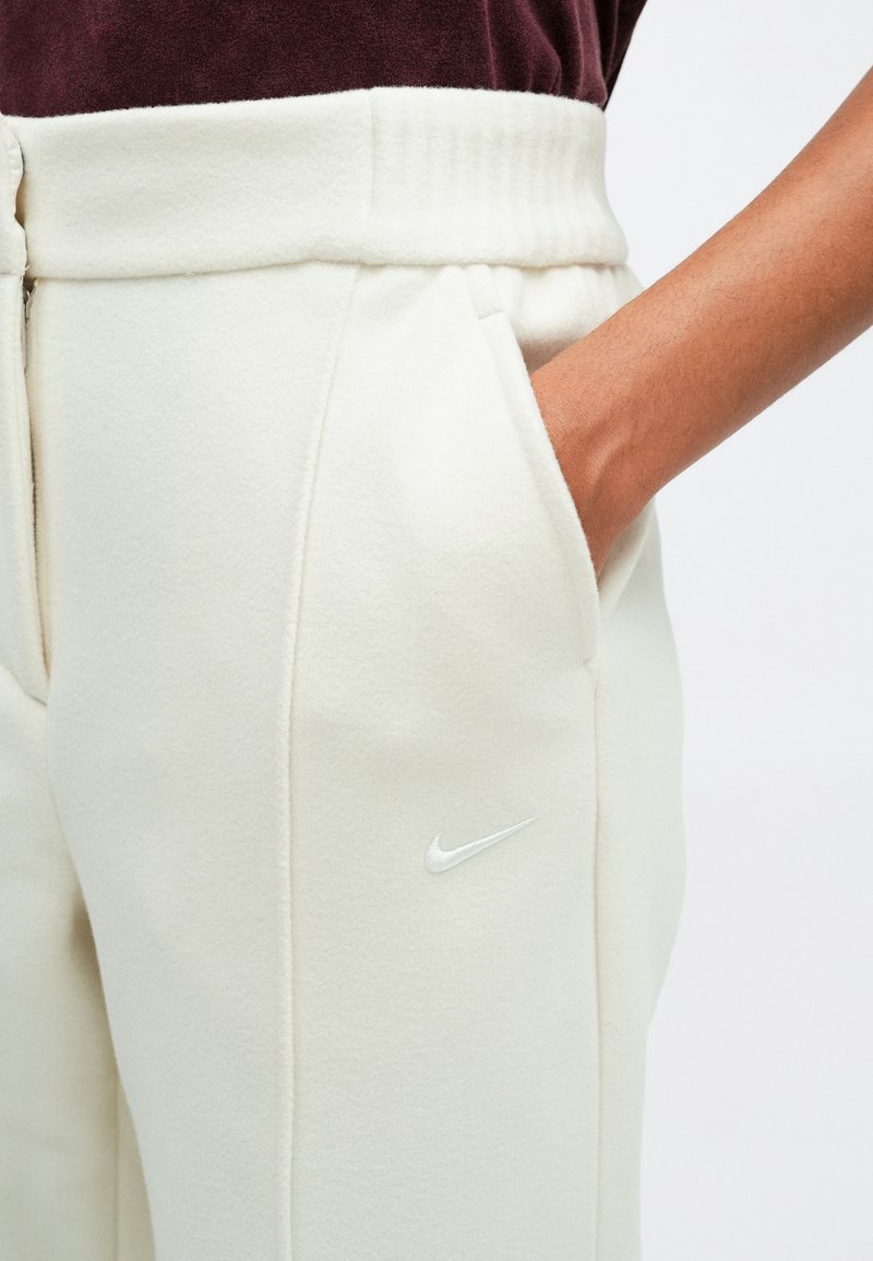 Helle cremefarbene Jogginghosen aus weichem, strukturiertem Stoff. Mit einem elastischen Bund, seitlichen Taschen und einem weißen Nike-Logo auf dem Oberschenkel.