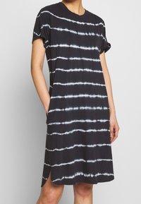 Black short-sleeve dress with white tie-dye stripes, made from soft fabric. Features a relaxed fit and pockets on each side.