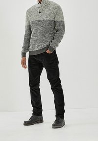 Gebreide grijze en witte trui met een hoge kraag en twee knopen, gecombineerd met zwarte ribfluwelen broek en donkere veterlaarzen.