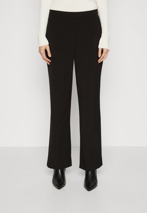 Black, wide-leg trousers with a smooth texture and elastic waistband. Paired with pointed black ankle boots, creating a streamlined silhouette.