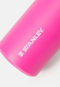 Ružičasti stainless steel tumbler s mat teksturom i bijelim logotipom "STANLEY". Cilindričnog oblika, dizajniran za izolaciju napitaka.