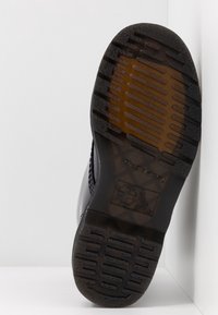 Semelle de chaussure en caoutchouc noir avec motif de bande de roulement texturé et gravure de la marque. Comprend des informations sur la résistance à l'huile, au glissement et au combustible.