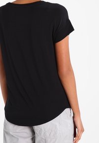 Svart kortärmad skjorta med rundad nederkant. Mjuk tyget hänger löst över kroppen. Upprullade ärmslutar ger en avslappnad detalj.