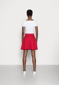 Jupe évasée rouge à taille haute, fabriquée en tissu doux, associée à un t-shirt blanc et des baskets blanches. Texture lisse, design arrivant au genou.