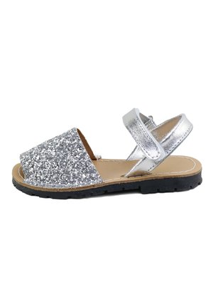 Sandalia infantil plateada con brillo, abierta en la punta, con tira en el tobillo y suela de goma negra sobre fondo blanco.