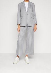 Szary garnitur w prążki z marynarką na jeden guzik i szerokimi spodniami, zestawiony z białymi masywnymi trampkami i gładką białą koszulką.