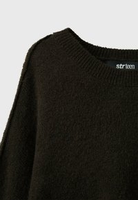 Gros plan d'un pull en maille texturée marron foncé avec col rond côtelé et étiquette de marque visible à l'intérieur du col.