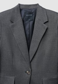 Grauer maßgeschneiderter Blazer mit Fischgrätenmuster, zwei Vorderfächern, Reverskragen und einem knöpfbaren Verschluss. Das Etikett trägt die Aufschrift "CALLIOPE."