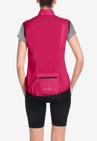 Gilet da ciclismo senza maniche rosa in tessuto leggero, dotato di una tasca posteriore con cerniera nera e maglietta grigia a maniche corte sotto.