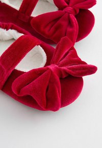 Pantofole di velluto rosso con grandi dettagli a fiocco, morbida fodera bianca e suole piatte. Presentano una cinghia per una vestibilità sicura.