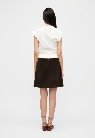 Λευκό τοπ με κοντά μανίκια και πτυχωτή υφή, συνδυασμένο με σκούρο καφέ φούστα A-line από σουέντ και καφέ παπούτσια με λουράκια, από πίσω.