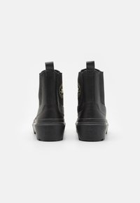 Botas de tobillo de cuero negro con paneles laterales elásticos, punta redondeada y suela de goma. Parche de logo notable en el lado exterior. Diseño simple.