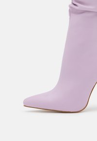 Botte à talon haut à bout pointu en matériau lavande doux avec une texture lisse et une silhouette courbée, dotée d'une semelle beige.