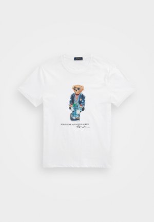 Biała koszulka bawełniana z nadrukiem graficznym przedstawiającym niedźwiedzia w okularach przeciwsłonecznych i niebieskiej marynarce, w paskowaną koszulę i niebieskie dżinsy.