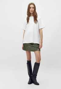 T-shirt bianco oversize abbinato a una mini gonna verde con paillettes, stivali neri al ginocchio e calze scure. Tessuto liscio e texture lucida.