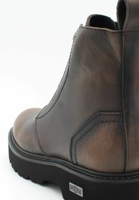 Stivale alla caviglia in pelle marrone con finitura testurizzata, punta arrotondata, zip laterale e suola in gomma nera con scanalature per la trazione.