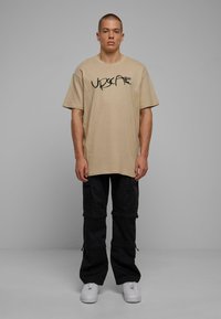 Beige oversized t-shirt with black text, paired with black cargo pants featuring pockets and zippers, completed with white sneakers.