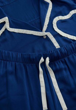 Blaues Schlafanzugset mit weißen Rüschendetails am Kragen und einer herzförmigen Tasche, mit einem elastischen Bund mit Kordelzug und einer Knopfleiste.