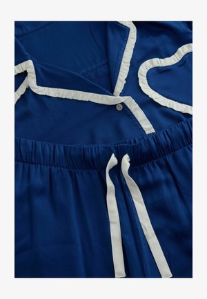 Modra pižama s belimi volančki ob ovratniku in žepu v obliki srca, z elastičnim pasom na vezanje in gumbom za zapiranje.