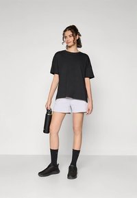 Čierne bavlnené tričko, voľného strihu, krátke rukávy. Kombinované s ľahkými fialovými šortkami. Drží čiernu fľašu na vodu, nosí čierne tenisky a ponožky.