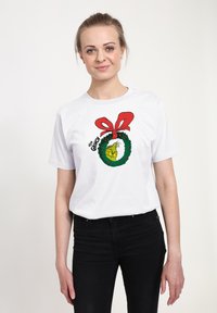 Bílý tričko s krátkým rukávem s designem zeleného věnce s červenou mašlí a textem "Grinch". Měkká bavlněná tkanina s klasickým střihem.