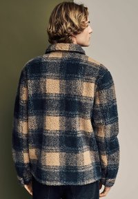Fleece bunda v námorníckej modrej farbe s béžovým kockovaným vzorom, s golierom a textúrovanou látkou; zobrazené zozadu.