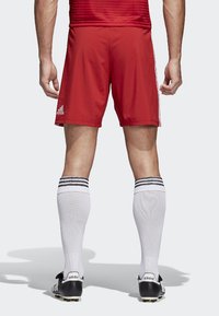 Rote Fußballshorts mit elastischem Bund, weißen Streifen an den Seiten, kombiniert mit knielangen weißen Socken mit schwarzen Streifen und schwarzen Fußballschuhen.