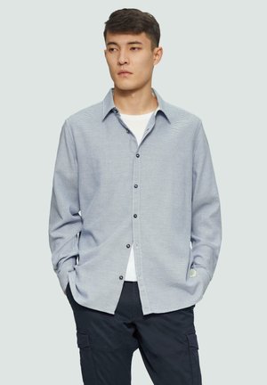 Overhemd met een gestructureerd blauw-wit patroon, lange mouwen en een kraag; gecombineerd met donkere broeken.